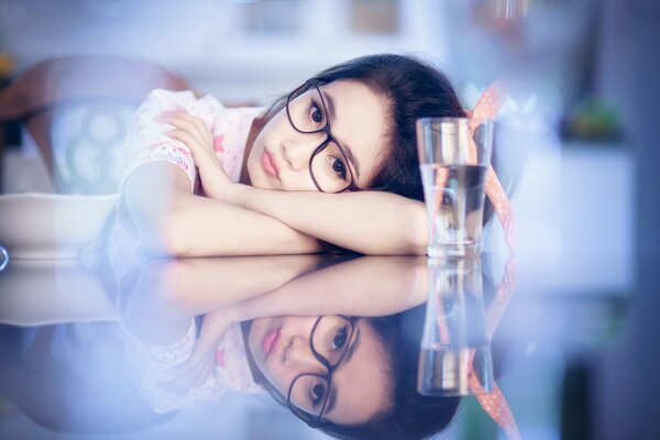 A girl with glasses on a blue background and a glass of water