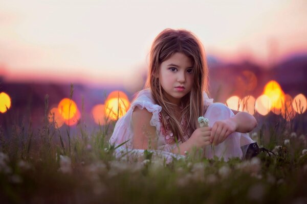 The girl is sitting on the field, with flowers in her hands