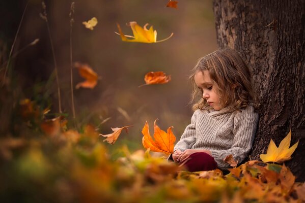 Una niña bajo un árbol con hojas en sus manos