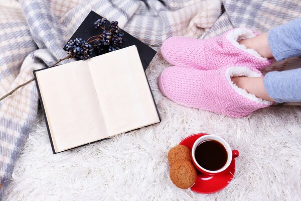 Les jambes de la jeune fille dans la maison rose Uggs. Tasse rouge avec café sur soucoupe rouge. Biscuits à l avoine. Livre ouvert. Plaid chaud à Carreaux et tapis blanc avec une grande sieste