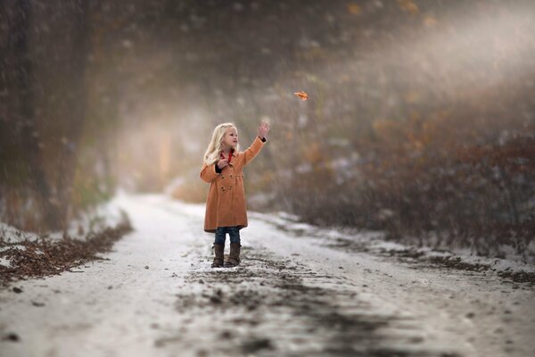 A girl stands on a snowy road and catches a leaf