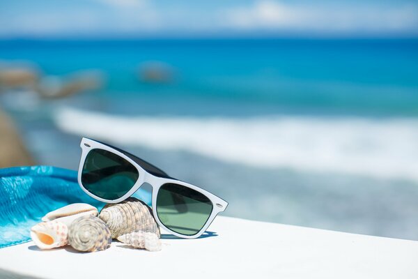 Lunettes de soleil, coquillages, paréo bleu sur banc blanc. Mer