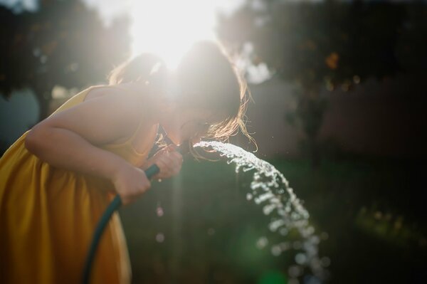 A girl drinking water from a hose in summer