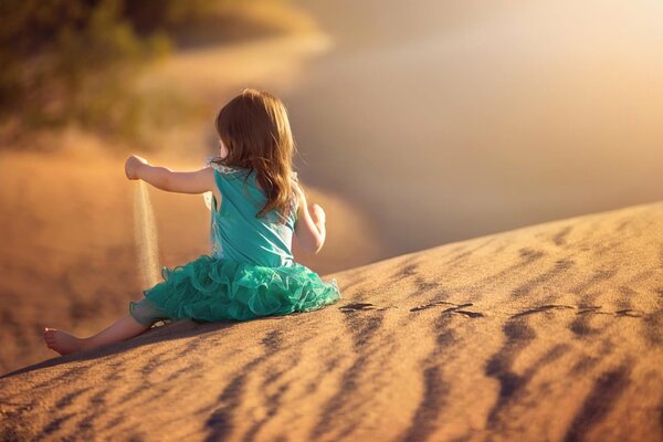 Mädchen im türkisfarbenen Kleid spielt mit Sand