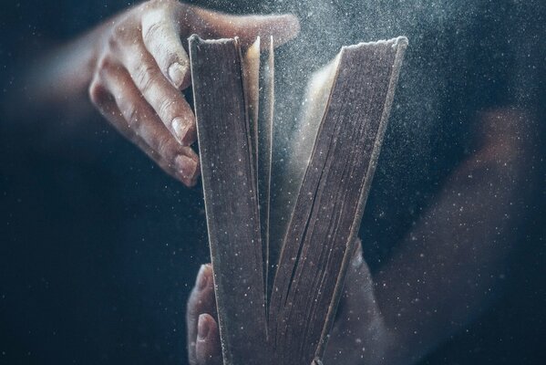 Hands holding an old book from which the dust flies out