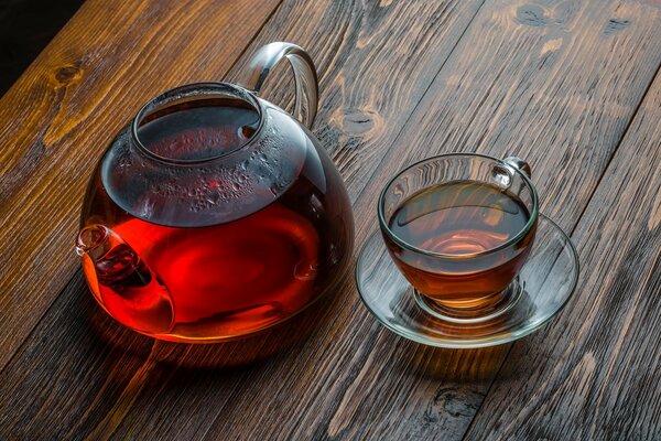 Tetera de vidrio con taza de té en la mesa