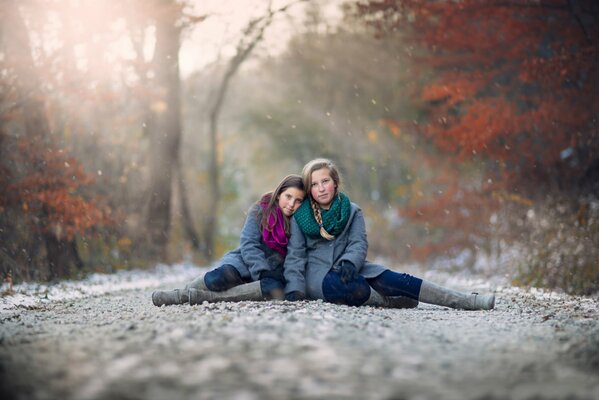 Girls sit sideways in the snow in autumn