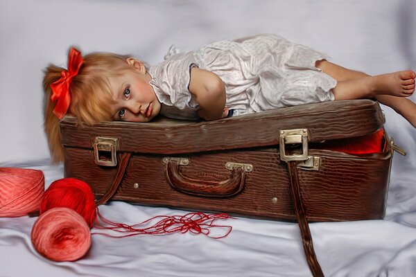 A little girl with a red bow is lying on a suitcase