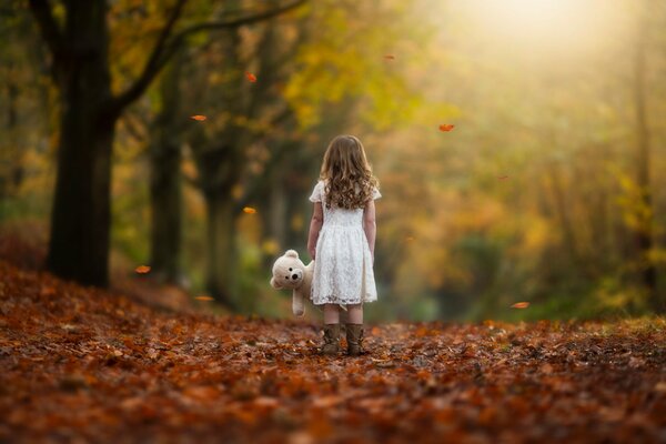 A girl with a teddy bear on autumn leaves