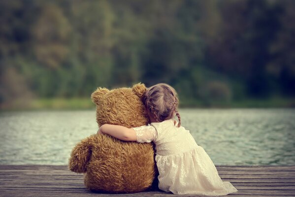 A girl on the background of a lake hugs a bear