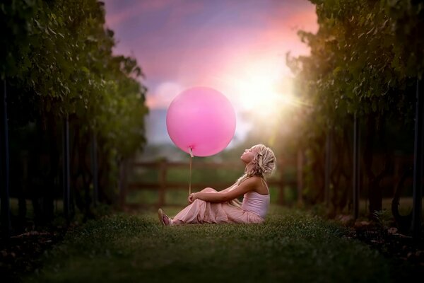 Drôle de fille assise sur l herbe et tenant une boule rose