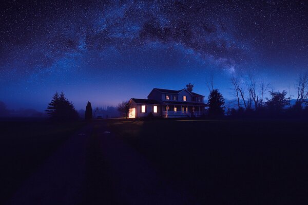 Maison avec fenêtres brûlantes et ciel étoilé nocturne