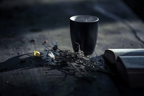 Flores con una taza en la mesa junto con un libro