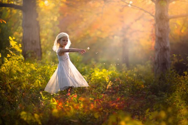 A girl in a dress blows a dandelion into the wind