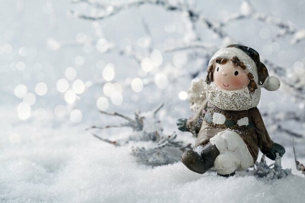 A toy in the form of a girl is standing in the snow, and behind the white lights