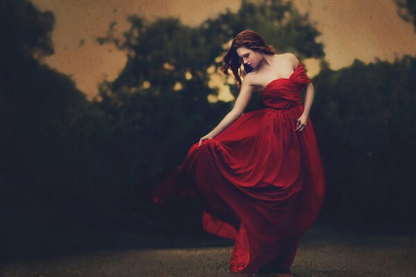 A girl in a red dress poses on a dark background