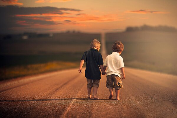 Two little boys walking barefoot on an empty road