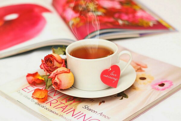 Tazza di tè su una rivista circondata da petali di rosa