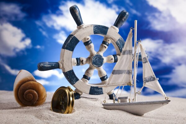 Shell, compass, rudder and boat on the sand