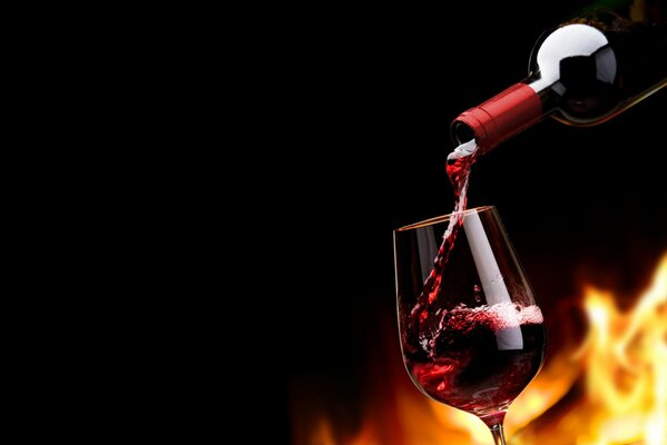 A bottle of red wine pours wine into a glass behind the flame