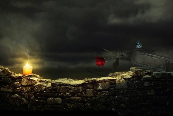 A candle, a butterfly and a red rose in a bottle on a stone fence at night