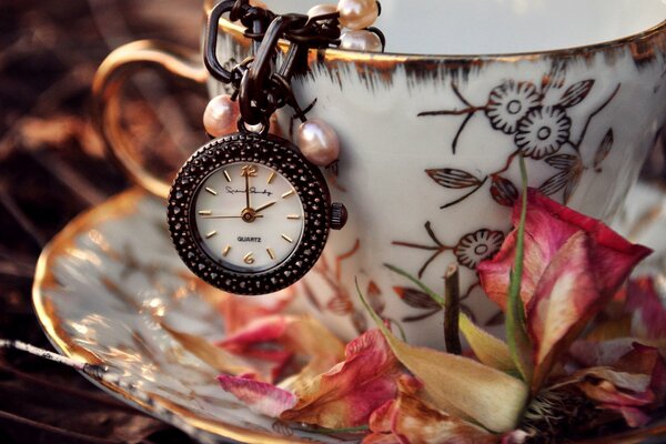 Cup and saucer inside with clock and rose petals on the ground