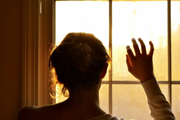 Ragazza, con la mano alzata, guardando fuori dalla finestra