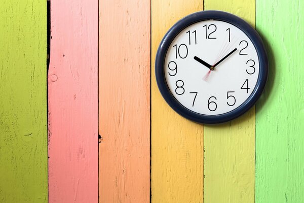 The clock is hanging on a multicolored fence