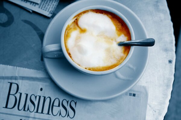 A mug of coffee with cream on the background of a newspaper