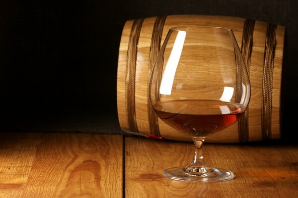 A glass of red wine at the bottom next to an oak barrel lying on its side