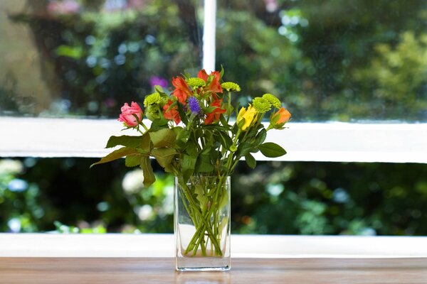 Blumenstrauß auf der Fensterbank vor dem Hintergrund des Fensters mit Grün