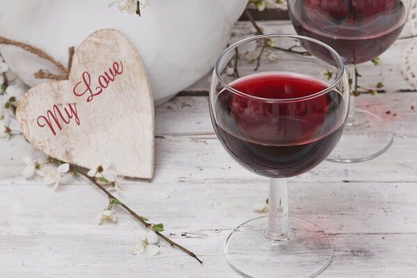 A glass of red wine with a wooden heart on a wooden surface