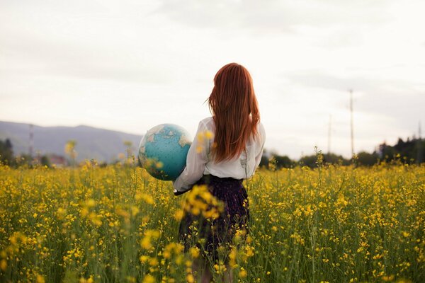 Photo of a red-haired girl with a globe in her hands in a field of rapeseed