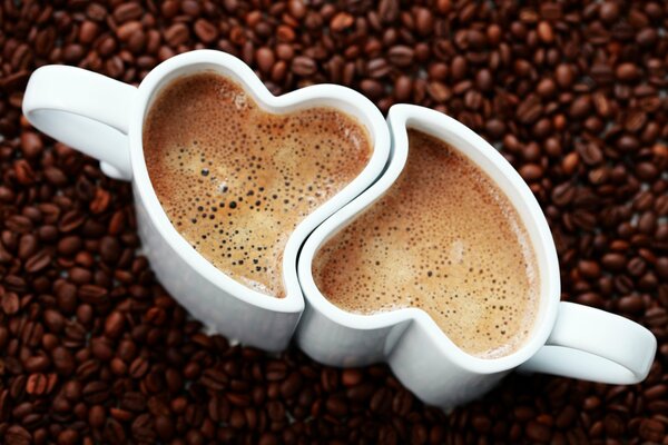 Two coffee mugs with a heart shape on the background of coffee beans