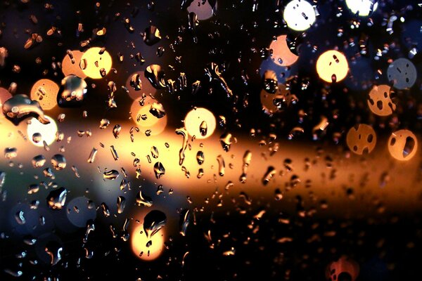 Drops of water on the glass run down against the background of lights