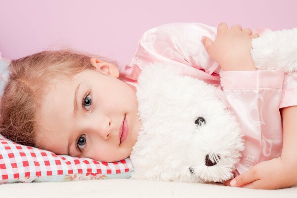 Imagen de una niña acostada en una almohada abrazada con un oso