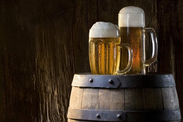 Two glasses of beer are on a gray barrel