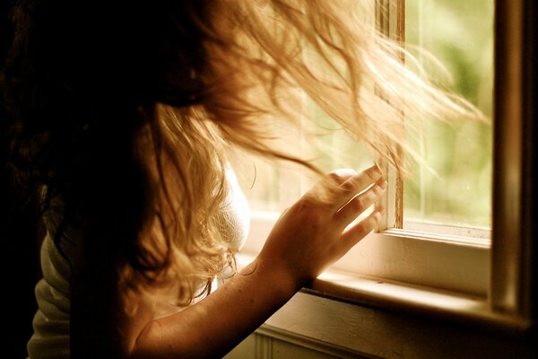 The girl with her hair disheveled looks out the window into the distance