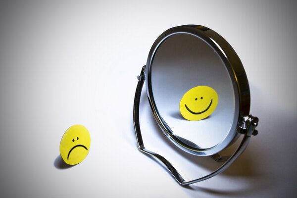 A sad smiley face is reflected in the mirror with a smile