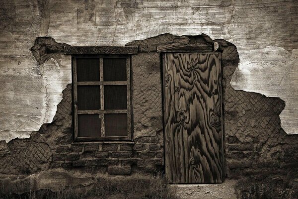 A dilapidated wall of an old house with a window and a door