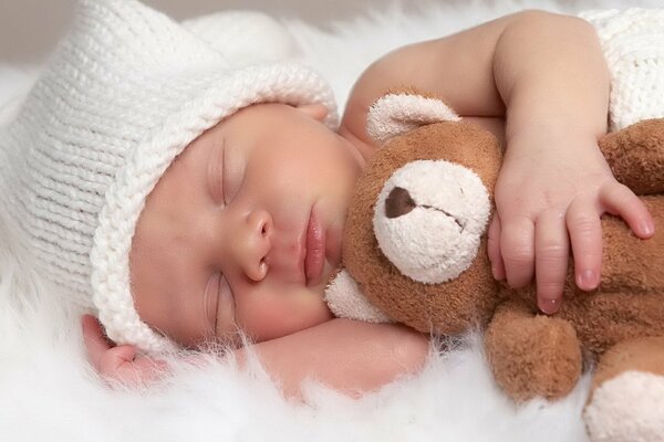 Schlafendes Baby in einer Mütze mit einem Teddybär