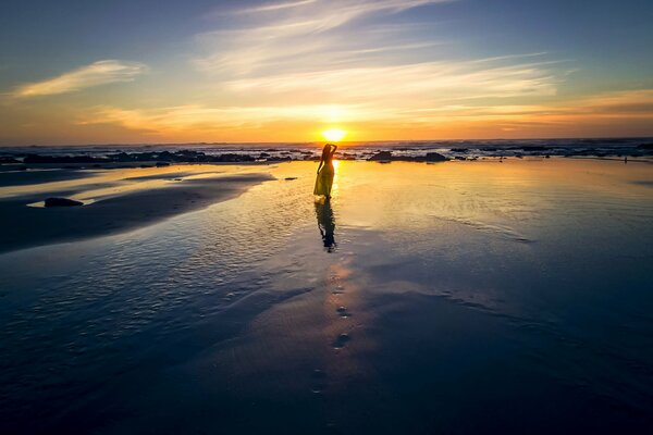 Ragazza in un vestito facile sulla spiaggia con il sole al tramonto