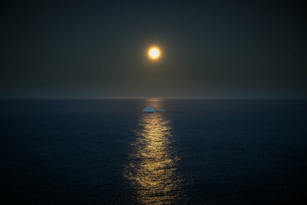 In mezzo al mare, un iceberg galleggia alla luce della luna piena