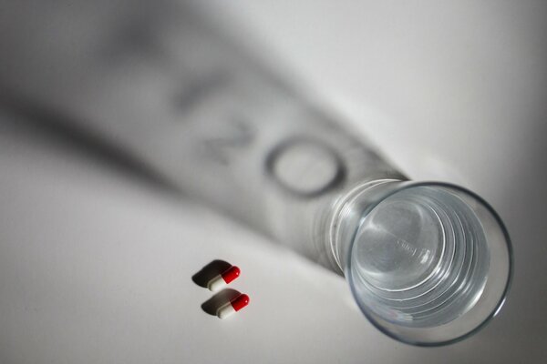 On the table is a glass of water and two pills next to it