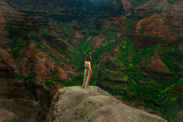 A girl in a multicolored skirt looks at a mountain landscape