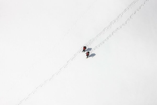 Colpo dall alto, campo bianco nella neve, due persone che camminano lungo il sentiero