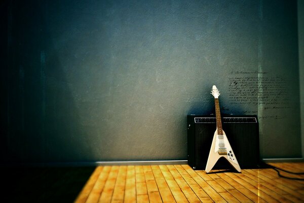 White electric guitar standing on the floor near the speaker