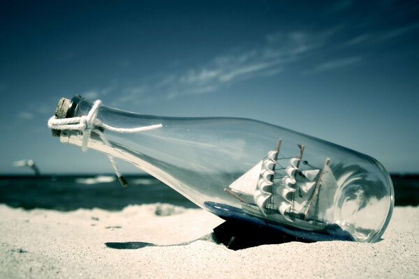 A bottle with a sailboat inside lies on the sand