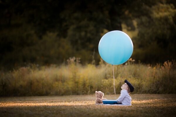 A boy with a teddy bear looks at a balloon