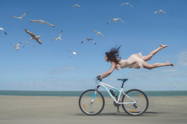 A girl flies over a bicycle on the seashore with seagulls